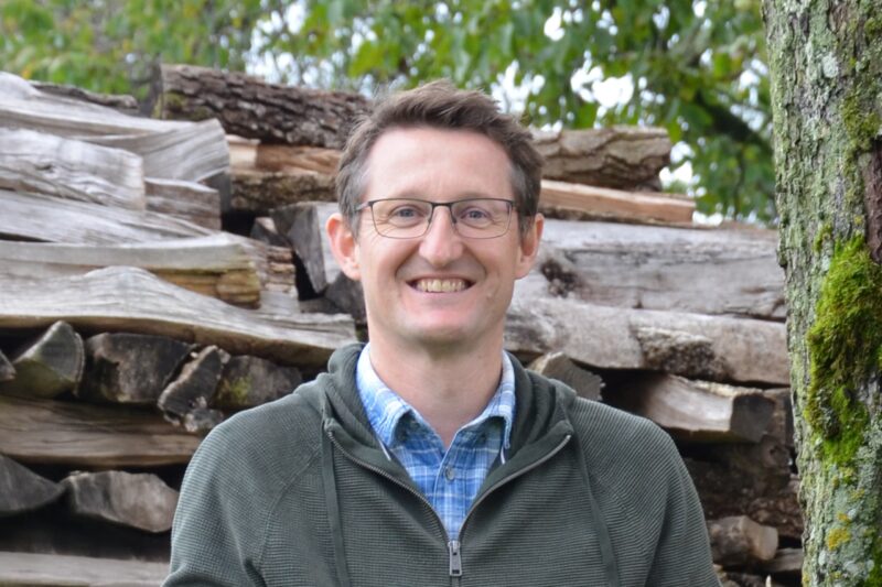 Portrait von Rainer Silber vor einem großen Holzstoß.