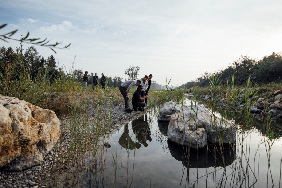 Eine kleine Gruppe Menschen stehen und knien an einer Wasserfläche.