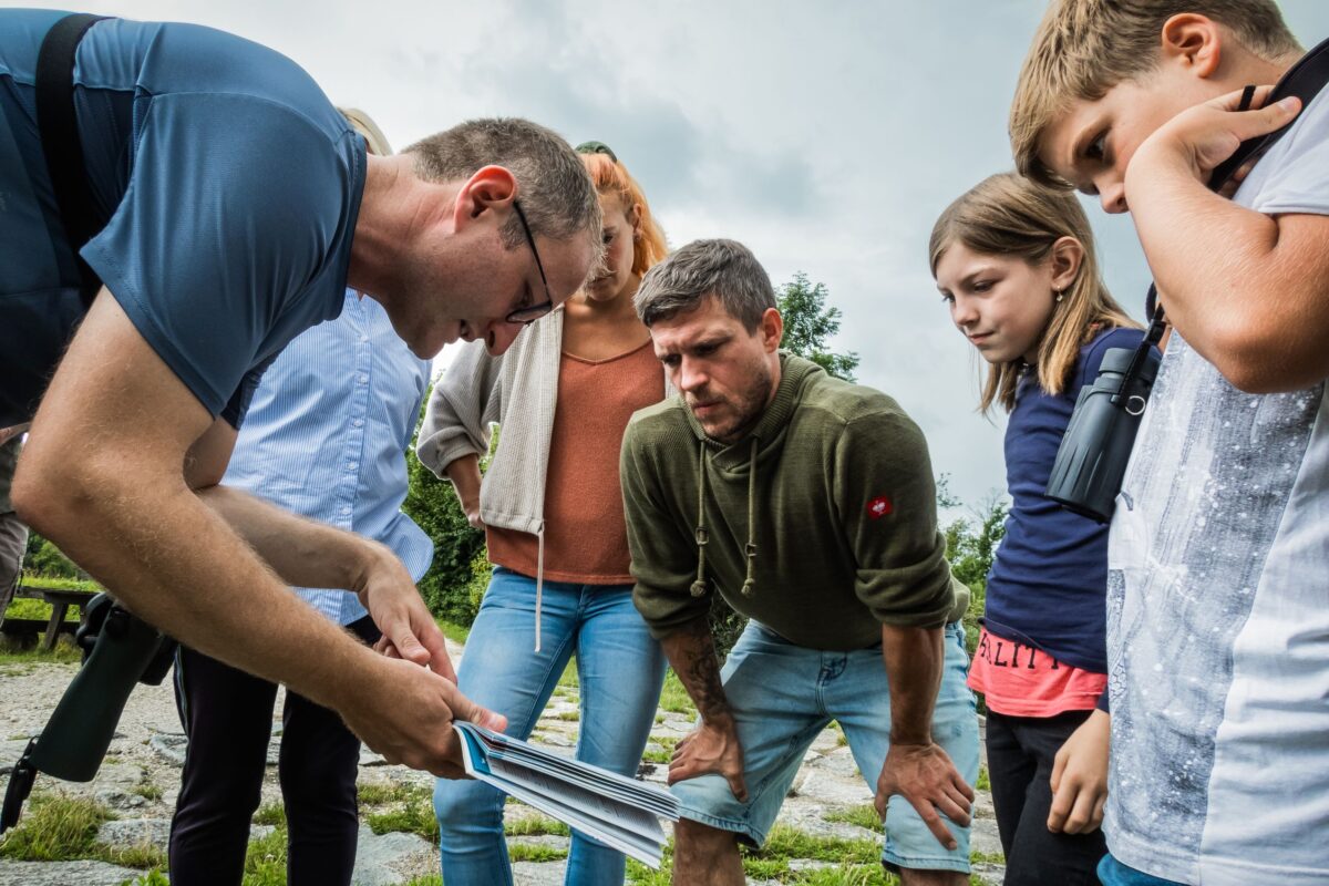 Ein Guide erklärt anhand eines Schaubildes, Kinder und Erwachsene hören und schauen aufmerksam
